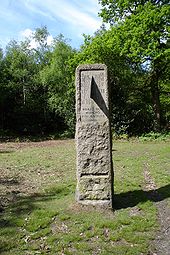 A standing stone in a grassy field surrounded by trees. The stone contains a vertical sundial centered on 1 o'clock, and is inscribed "HORAS NON NUMERO NISI ÆSTIVAS" and "SUMMER TIME ACT 1925".