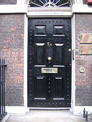 A black front door located on an old red brick building. There is a letter slot built into the door approximately 3 feet or 90 centimetres from the bottom.