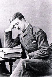 Druitt, a thin young man with dark hair parted in the middle and a small moustache, sits at a table and reads a book