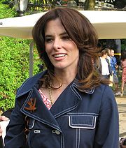 A smiling brown-haired woman wearing a blue denim jacket standing outside.