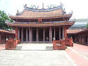 A religious temple. A one meter high stair leads to the ground floor. Two large pillars and six smaller ones supports a red tiled roof.