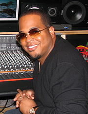 An African American man wearing glasses, sits smiling in a recording studio.
