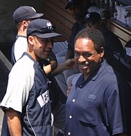 A man in a navy blue and grey windbreaker with the word "New" visible stands on the left facing a man in a navy blue polo shirt who is looking away.