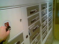 A number of letterboxes beside an electronic keyreader. A hand is holding an electronic key up to the reader, and one of the boxes is automatically opening.