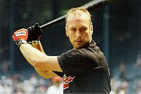A man in a black jersey and batting gloves prepares to swing the baseball bat that he is holding.