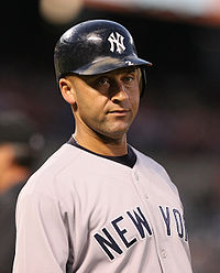 A man in a navy helmet and grey baseball uniform stares into the distance