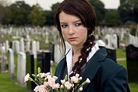 A portrait of April, a teenage girl dressed in a school uniform, walking through a graveyard, holding flowers