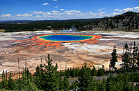 Pool of blue water surrounded by orange and yellow residue, in ashen rock basin.