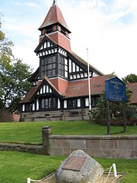 A church seen from the west showing timber framimg, brickwork, windows, and a tower with a lead spire