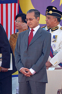 A photo showing former Prime Minister Mahatir bin Mohamad standing with head down and surrounded by government officials at the celebration of the 50th independence day.