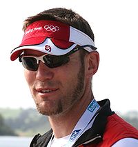 Headshot of Marcel Hacker sporting a red Beijing 2008 Olympic visor with black sunglasses.
