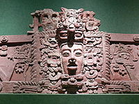 Section of stucco frieze with a prominent human face in the centre, surrounded by elaborate decoration.