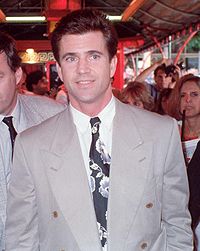 Mel Gibson, with dark brown hair, in a gray suit, white dress shirt, and black-and-white patterned tie.