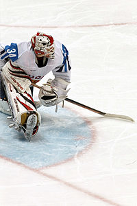 a goaltender in a blue and white uniform looks to his left as he stretches his legs