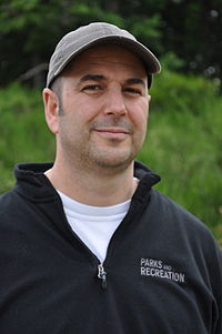 A man wearing a black fleece with the words "Parks and Recreation" on it, and a gray hat.