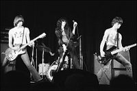 A black and white picture of a rock band with four members shown performing on stage.