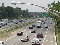 A six lane freeway lined with lampposts in a suburban area