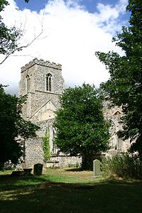 A flint church seen between trees, the body ruined and roofless, the tower with a battlemented parapet