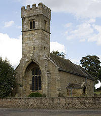 A stone church seen from the southwest with a prominent battlemented tower at the base of which is a recessed arch containing a large window