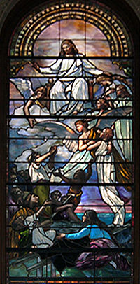 This stained-glass window shows two angels carrying a small child up towards Christ seated on golden clouds in while a group of people below are watching.