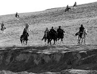 Ten horses with riders on the side of a hill