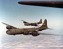 Two large, olive-colored aircraft flying over farmland.