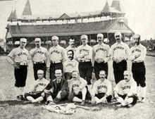 Two rows of men: one row standing behind a second row seated on the ground. The men are wearing white baseball uniforms with "Detroit" across the chest and white baseball caps.