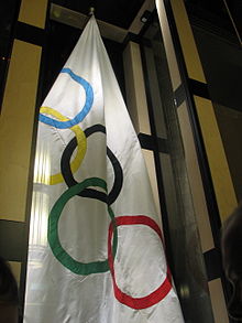 White flag hanging from the ceiling with the five interlocking rings symbolic of the Olympic Games. The rings are each a different color with blue, yellow, black, green, and red.