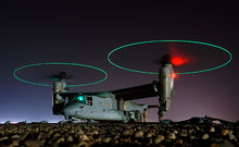  Ground crew refuel an MV-22 before a mission in central Iraq at night. The rotors are turning and the tips are green, forming green circles.