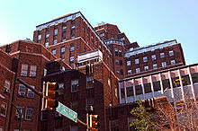 A red brick high-rise building with several wings and levels in front of a bright blue sky with a traffic light and street sign visible at the bottom.