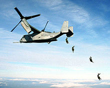 Four U.S. Marine paratroopers jump from the rear loading ramp of a MV-22 Osprey.