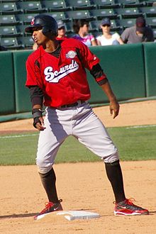 A man wearing a red baseball jersey with "Sounds" written across the chest, gray pants, and a black batting helmet stands on second base