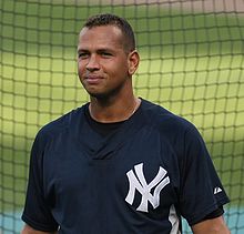 A baseball player stands in front of a screen. He wears a navy blue shirt with a white interlocking N and Y.