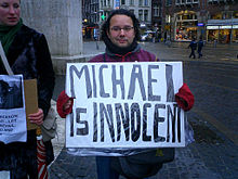 A man in a street holds a sign which reads "Michael Is Innocent"