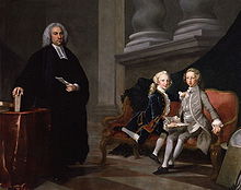 Conversation piece in oils: man dressed in black with a clerical collar stands beside two boys sitting on a settee, one wearing a grey suit the other a blue one. The man holds a sheet of paper; the boys hold a book.