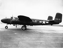 Black and white photo of an early bomber parked perpendicular to camera, facing left. Rearward of the wing is a star in front of horizontal stripes