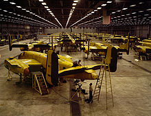 Interior of huge aircraft factory where rows of bombers covered in a yellow layer are manufactured.