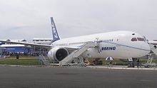 Front/side view of white 787 on static display. Stairway is positioned ahead of the right engine for access into cabin.
