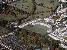 Aerial photograph of semicircular terrace of stone buildings with large expanse of grass in front and to the left. Also shows surrounding terraces of buildings.