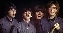 The Beatles, wearing identical dark-grey button-down shirts. They are clean-shaven, except for Starr, who has a moustache. Lennon, wearing mutton chops, holds a folded telescope. All are smiling, except for McCartney, who looks pensive.