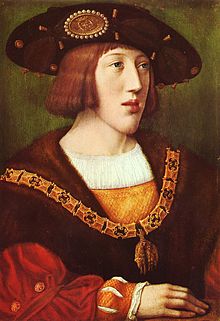 A young noble with brown hair and a long chin, bedecked in fine clothes and a hat.
