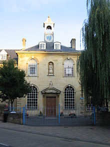 Yellow stone building with central 2 storey block with arched windows, hipped roof and clock tower