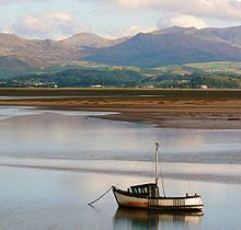 A fishing boat at anchor in the estuary, with mudflats and mountains in the background