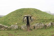 A low grassy mound with an entrance at its centre framed by cyclopean stones