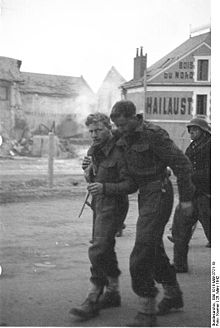 two British soldiers one appears wounded being helped by his comrade with a German guard in the background