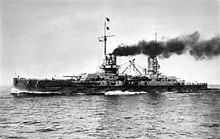A World War I-era battleship at sea; her two funnels are emitting a large amount of smoke