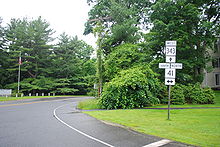 An intersection of two two-lane highways in a wooded residential area. A sign assembly in the foreground indicates that Connecticut Route 343 is straight ahead while Route 41 is accessed by turning to the left or right.