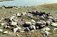 Photograph of a circular arrangement of rocks on open ground with a body of water in the background