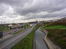 View from a bridge over a canal, with a motorway running to the left. The sky is dark and overcast.