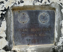 A grey plaque on a white surface with evidence of chipped paint and general decay